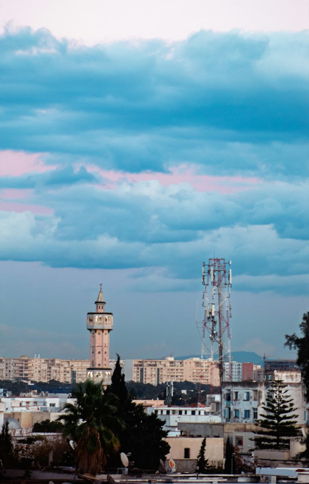 A city skyline with a cell tower rising above the rooftops