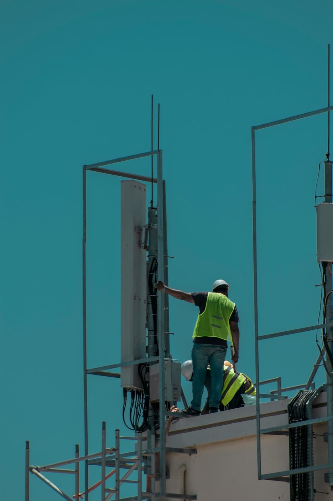 Two technicians in high-visibility vests working on a cell site